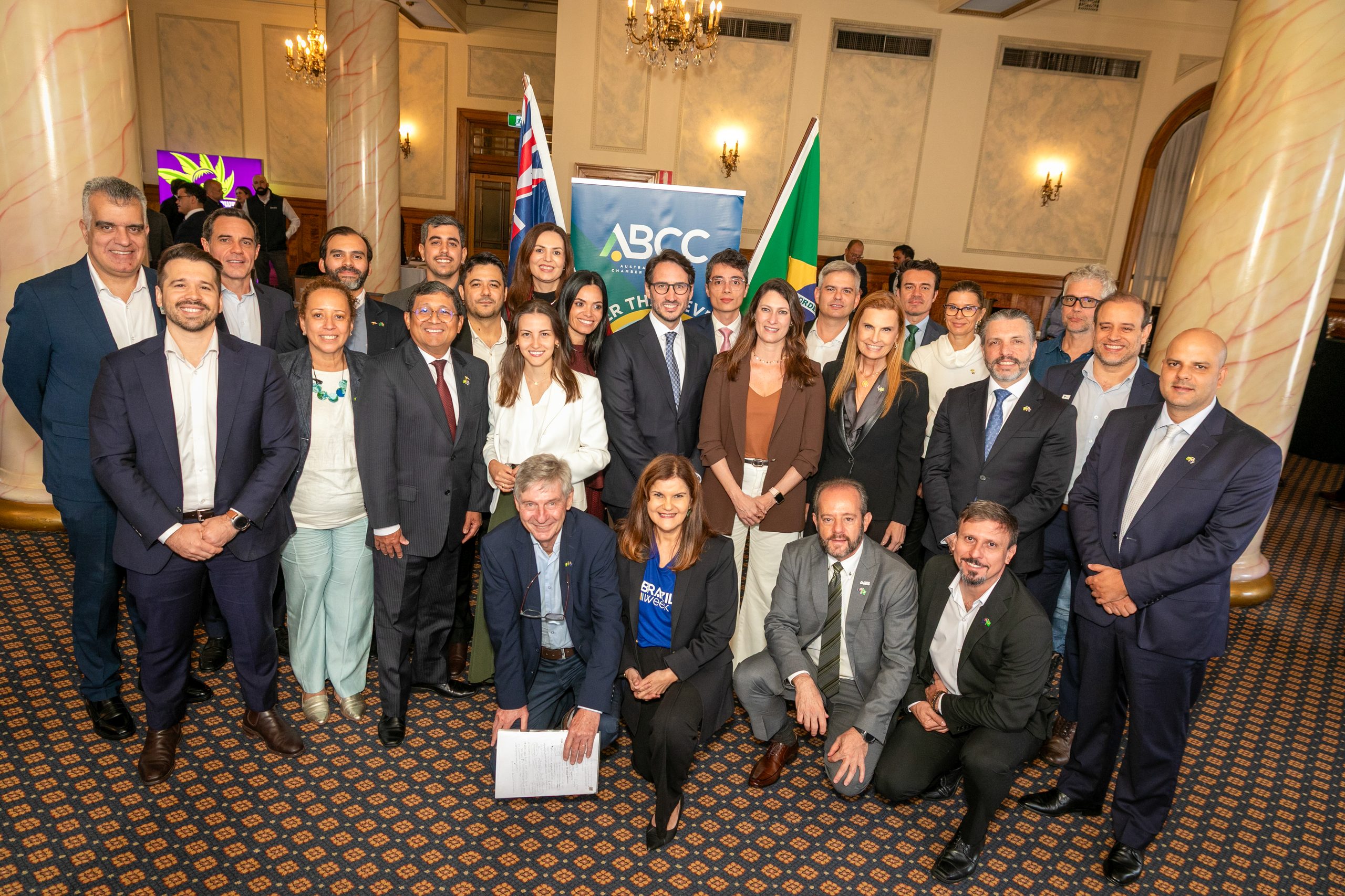 Large group of participants posing in front of a banner and the flags of Brazil and Australia.